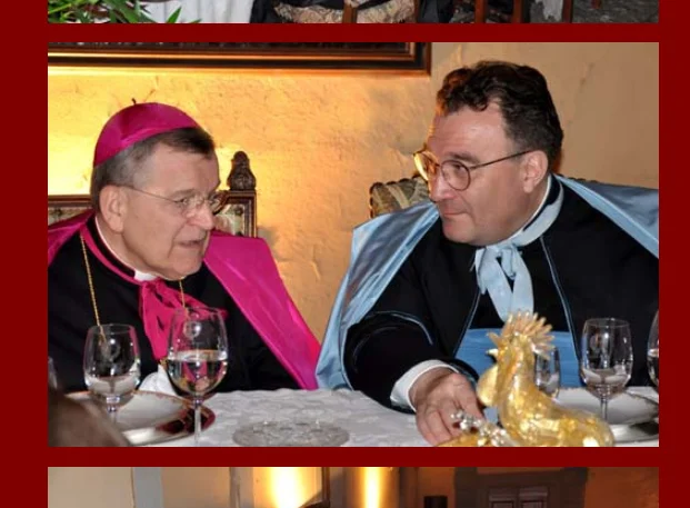 Le cardinal Raymond Burke et Mgr Gilles Wach, fondateur de l&rsquo;Institut du Christ Roi Souverain Prêtre, sont assis côte à côte à une table dressée. À gauche, le cardinal Burke porte la calotte, le rabat et le camail amarante réservés aux cardinaux. À droite, Mgr Wach est vêtu de l&rsquo;habit du chœur de son institut, reconnaissable à sa mozette bleu céleste. Tous deux, portant des lunettes, sont tournés l&rsquo;un vers l&rsquo;autre en pleine conversation.