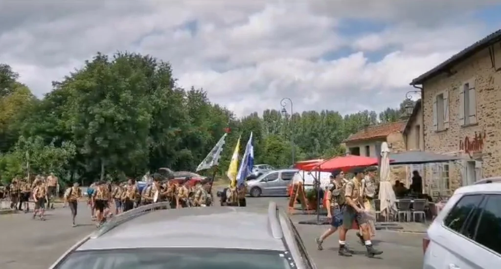 Défilé d'un groupe d'Europa Scouts dans une rue pavée de Solignac, avec deux porteurs de drapeaux en tête.