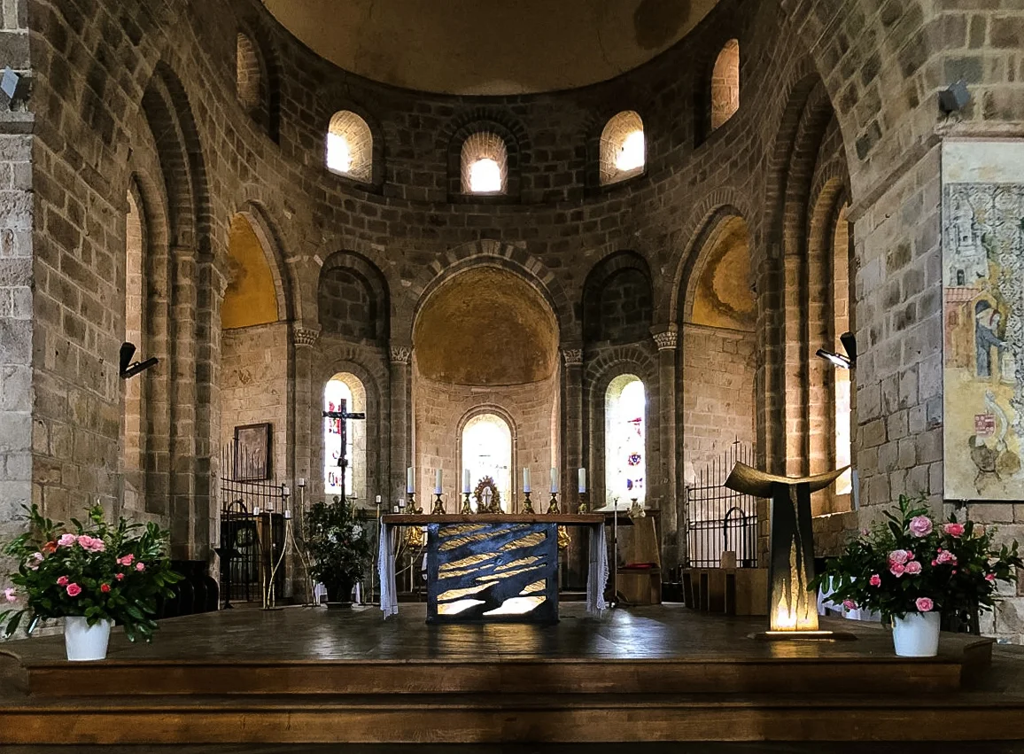 Vue en noir et blanc du chœur de l'abbatiale de Solignac, montrant l'aménagement intérieur avec l'ancien maître-autel au fond, des bancs alignés le long de la nef et la structure architecturale en pierre sous l'abside romane.