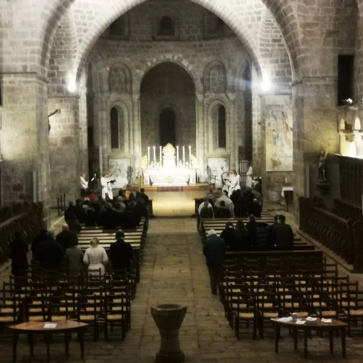 Intérieur de l&rsquo;église abbatiale Saint-Pierre-Sainte-Marie de Solignac lors d&rsquo;une célébration liturgique, avec quelques fidèles assis dans la nef face au chœur éclairé par des bougies.